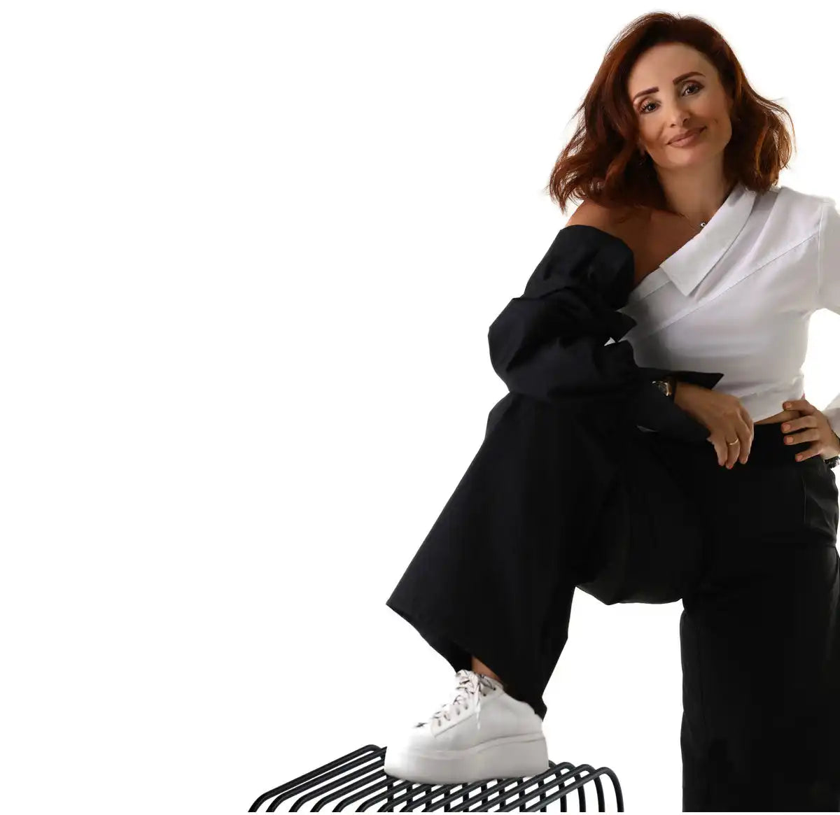 A person wearing a black and white outfit with white sneakers sits on a striped platform.