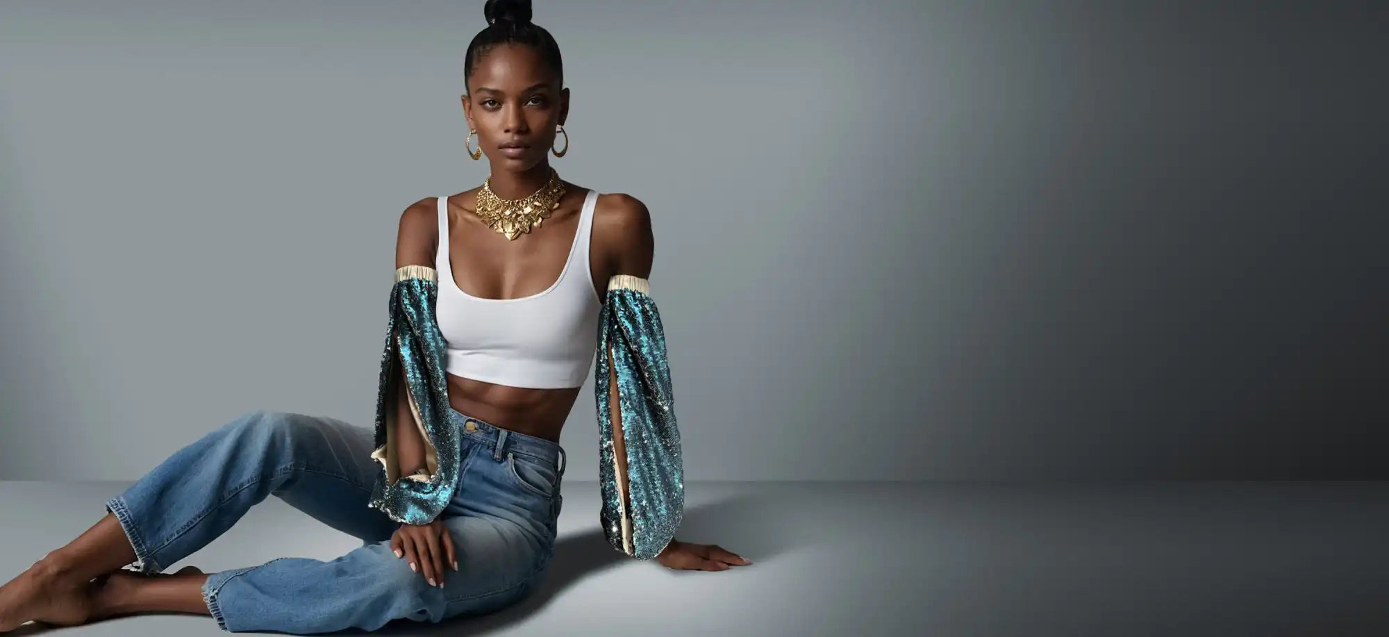 A person wearing a white crop top, teal cardigan and blue jeans sits casually on the floor.
