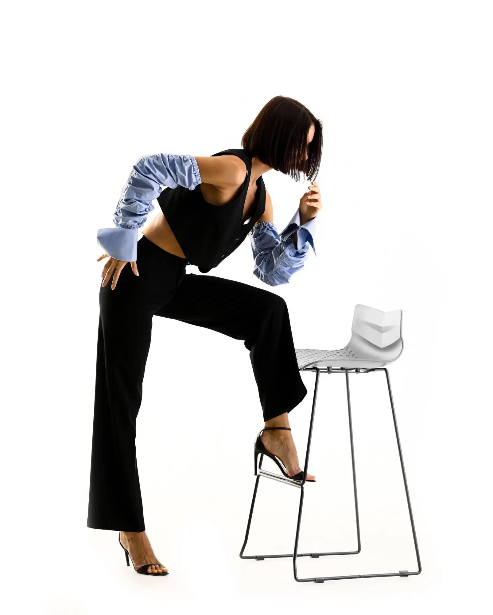 A dancer in black pants and striped sleeves strikes a dynamic pose beside a white bar stool.