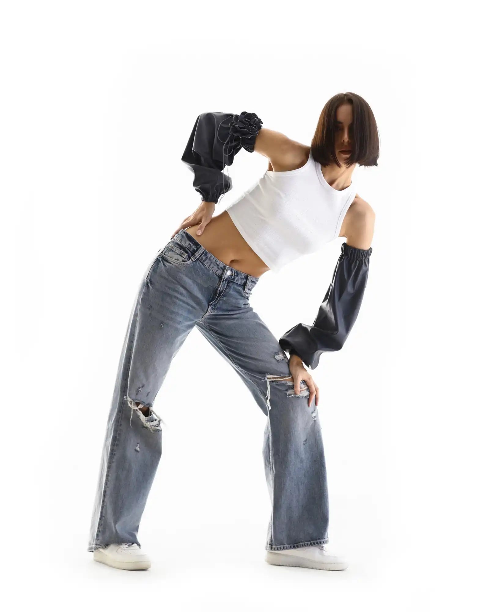 A dancer striking a dynamic pose while wearing ripped jeans and a white tank top.