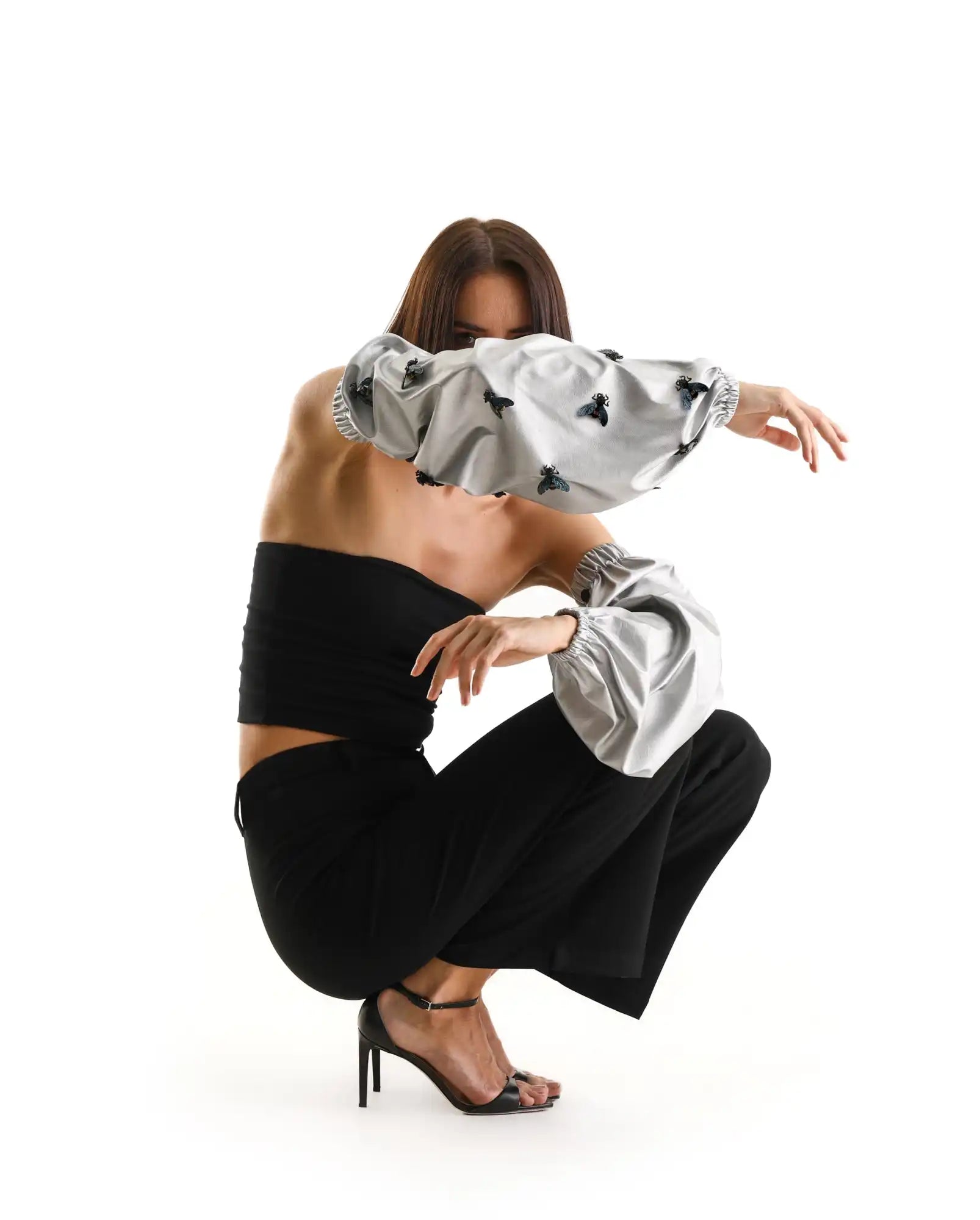 A dancer in a crouching pose wearing black pants and a silver top.