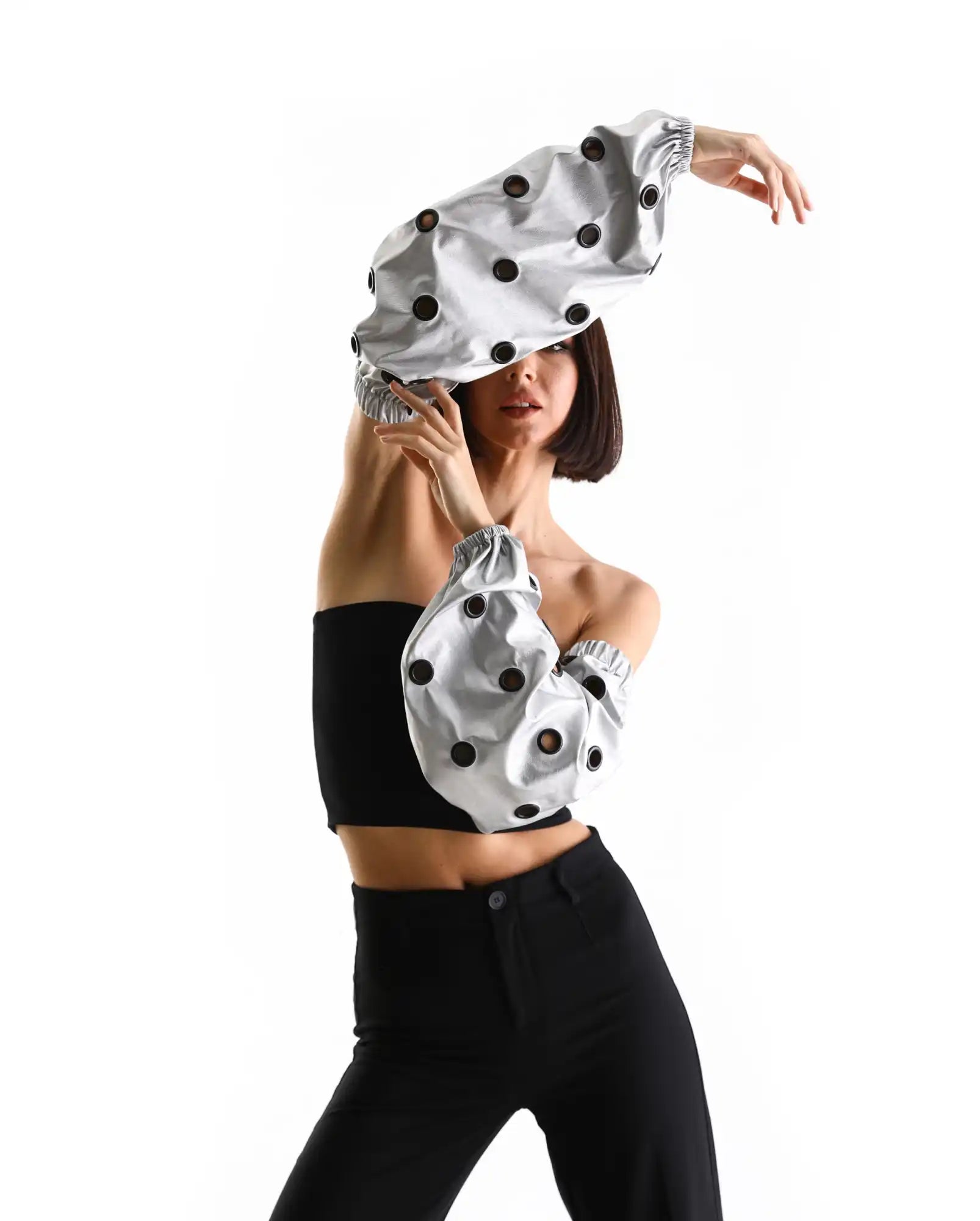 A polka-dotted silver hat and matching sleeve accessory worn with black attire.